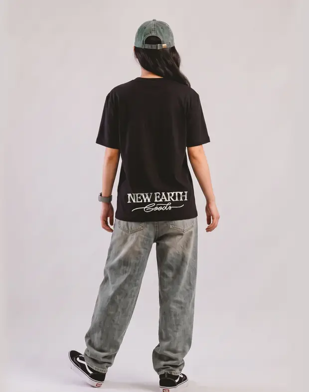 Modelo de boné e jeans claro de costas, com New Earth Goods estampado na camiseta preta