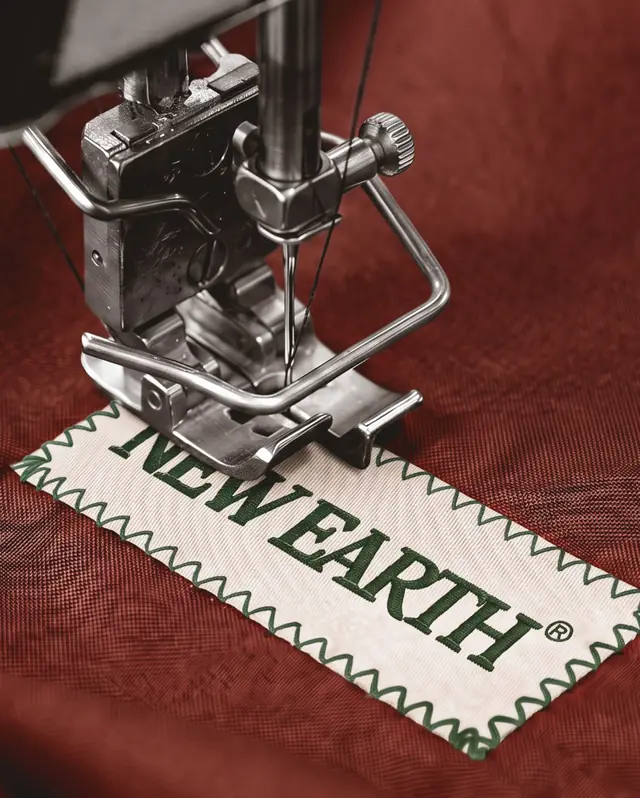 Máquina de costura pregando a etiqueta bordada NEW EARTH em um tecido vermelho